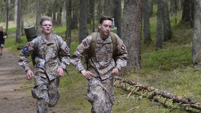 Rucking seriāla posms - jaunieši, tērpti militārajā apģērbā, skrien ar mugursomām