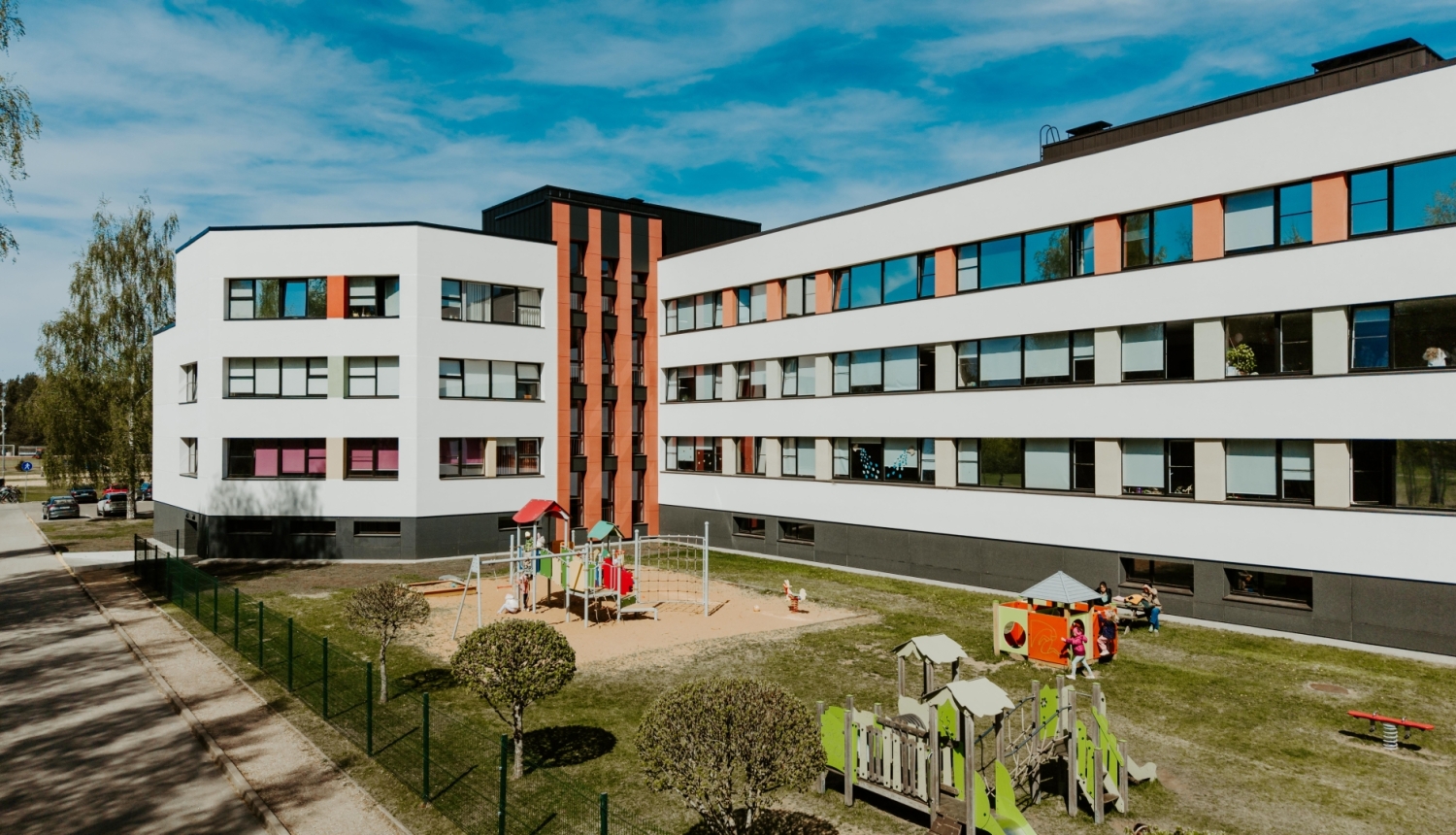 Atjaunots Ādažu vidusskolas D korpuss, balta ēka ar sarkaniem elementiem zilu debesu fonā