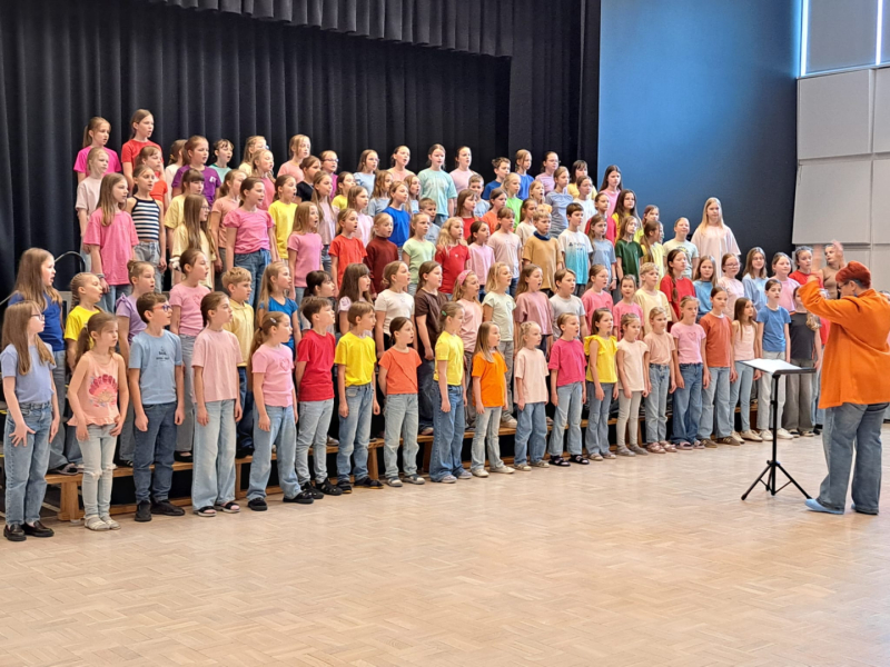 bērni dzied diriģentes pavadībā, bērni krāsaini ģērbti
