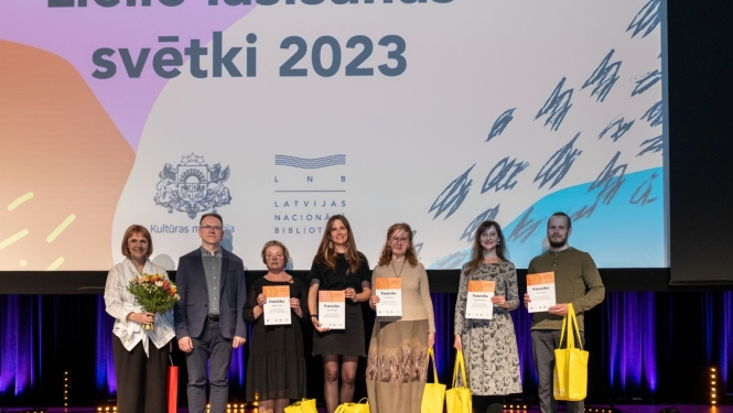 cilvēki stāv uz skatuves ar diplomiem rokās