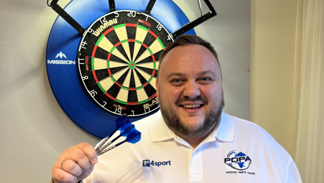 Jānis Dāmis tur rokā šautriņas, fonā šautriņu mešanas aplis