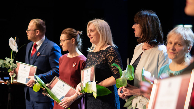 cilvēki ar ziediem un pateicības rakstiem uz skatuves