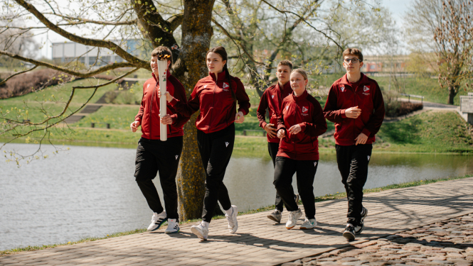 Jaunieši Latvijas izlases tērpos nes Latvijas Jaunatnes olimpiādes lāpu gar ezeru