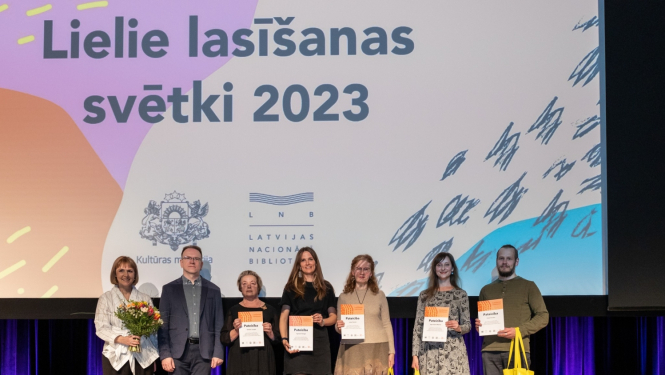 cilvēki stāv uz skatuves ar diplomiem rokās