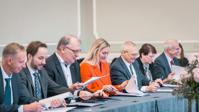 cilvēki pie gara galda paraksta dokumentus