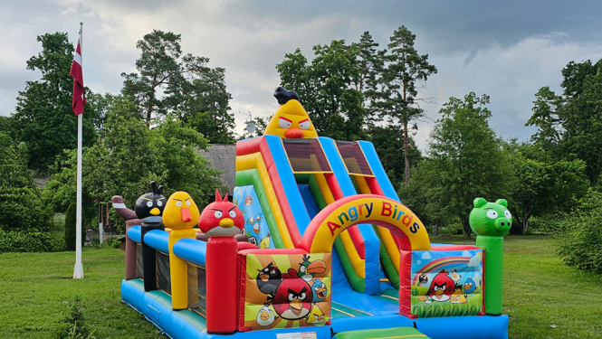 Piepūšamas atrakcijas, fonā Latvijas karogs, zāle un koki