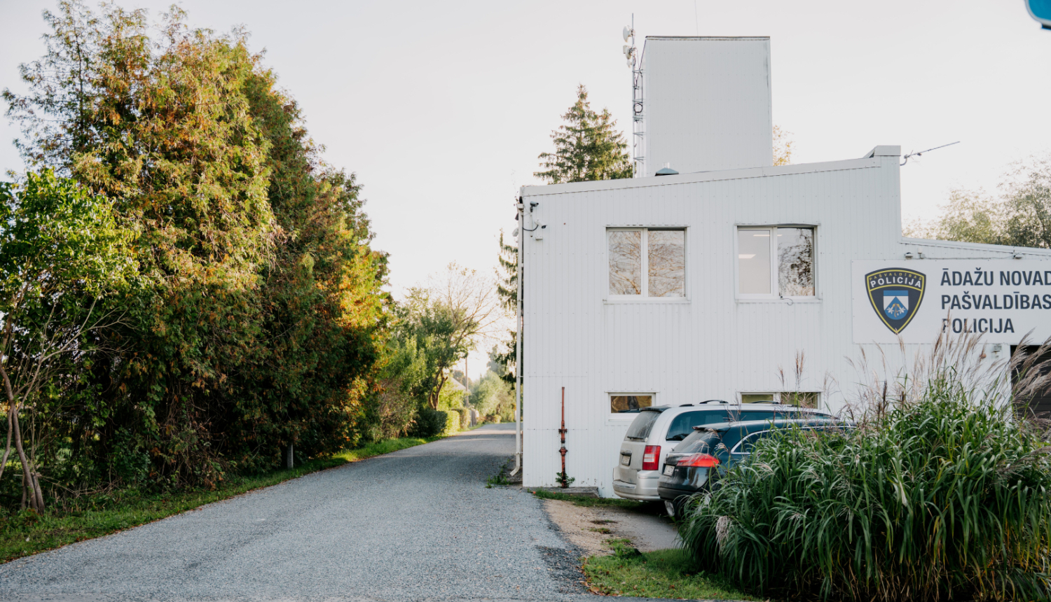 Ādažu novada pašvaldības policijas ēka, baltā krāsā, zaļojošu koku ieskauta