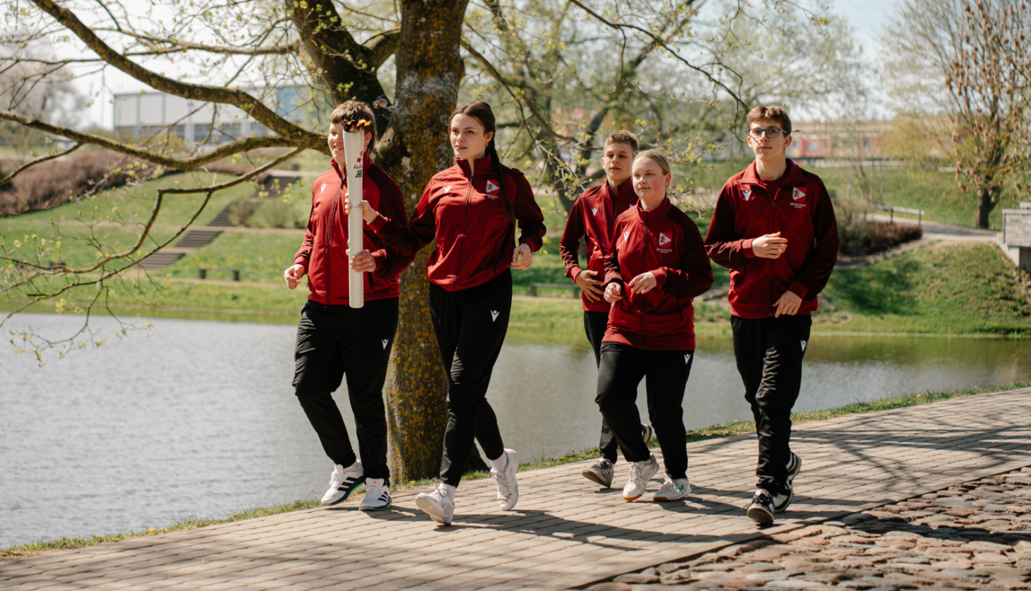Jaunieši Latvijas izlases tērpos nes Latvijas Jaunatnes olimpiādes lāpu gar ezeru