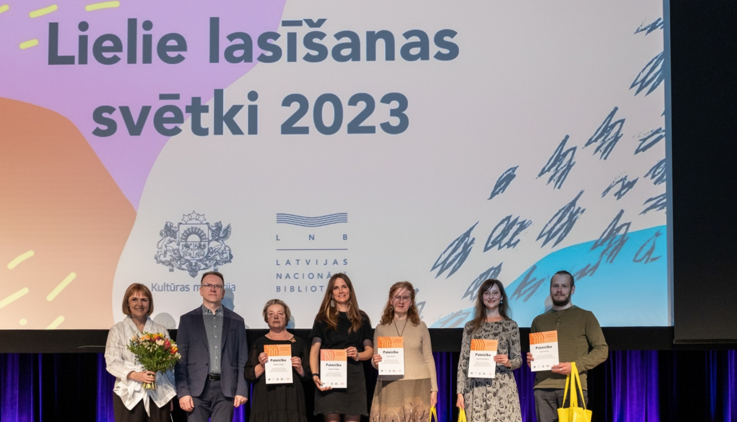 cilvēki stāv uz skatuves ar diplomiem rokās