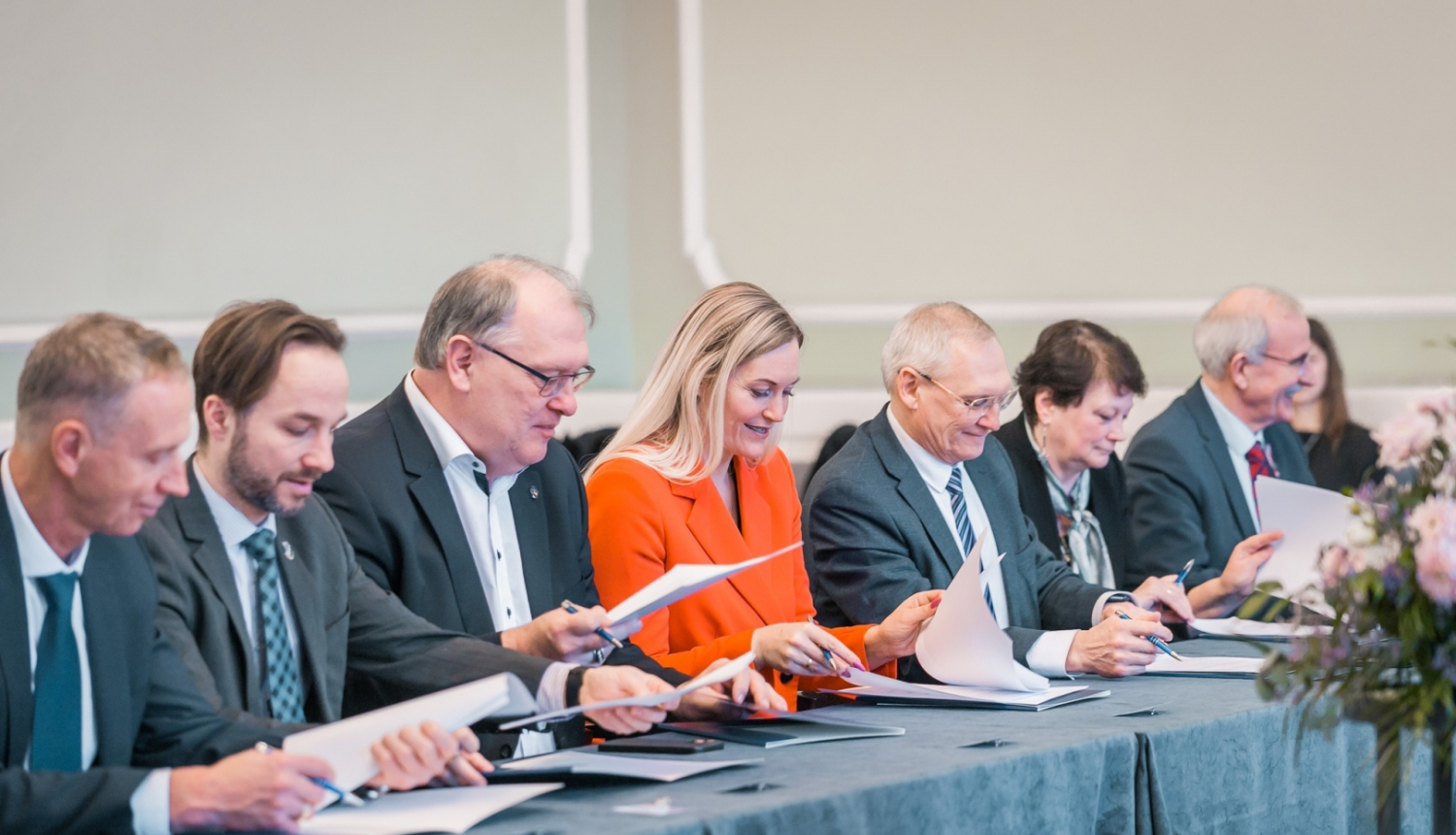 cilvēki pie gara galda paraksta dokumentus