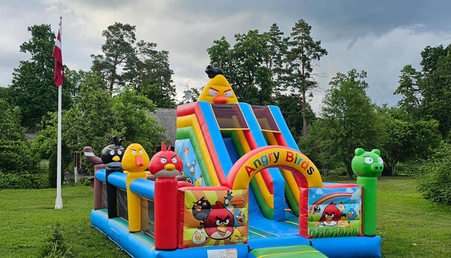 Piepūšamas atrakcijas, fonā Latvijas karogs, zāle un koki